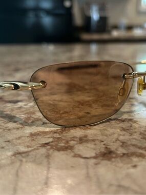 Oakley Why 8.0 sunglasses with brown lenses and gold accents.